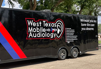 A black mobile audiology clinic on wheels with a sign on it that reads "West Texas Mobile Audiology"