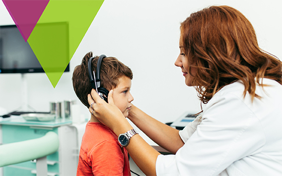 A woman audiologist places headphones on a young boy.
